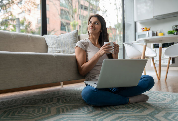 Woman sitting on floor with coffee and laptop