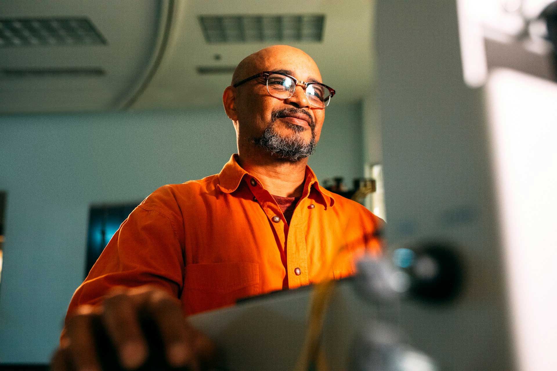 Happy bald man with bright orange shirt standing in front of a computer.
